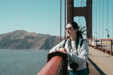 sırt çantası kadın fotoğrafçı zevk güzel doğa görünümü üzerinde golden gate köprüsü san francisco Kaliforniya ABD. Genç kız taşıma kamera itimat defne okyanus mavi su gezi kırmızı küpeşte.