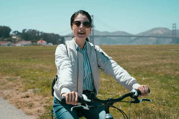 golden gate köprüsü güneşli arka planda ile olumlu mutlu kız binmek bisiklet park. Açık havada Bisiklete binme güneş gözlüğü takıyor kameraya gülümseyen genç erkek. güzel Bayan seyahat gezi.