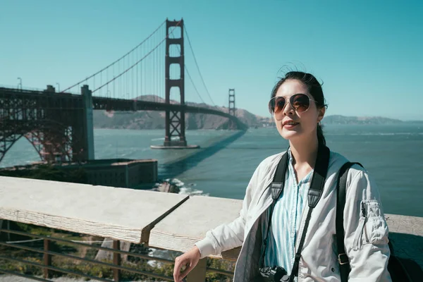 golden gate köprüsü arka planda ile ahşap Küpeşte güvenerek çekici gülümseme ile güneş gözlüğü takmış kız yüz kamera odaklanmak. Genç kadın backpacker seyahat Tur Amerika yaz aylarında gezi.