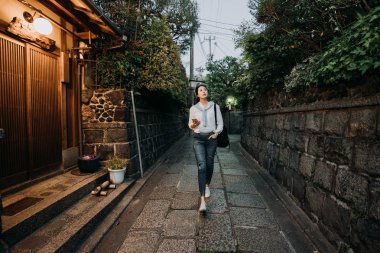 tam uzunlukta yalnız eski tarihi şehir kyoto Japonya'da küçük yolunda yürüyen genç kız ziyaretçi. cep telefonu Ishibe sokakta otel bulma tutan Bayan gezgin. Güzel Asyalı kadın rahatlatıcı.