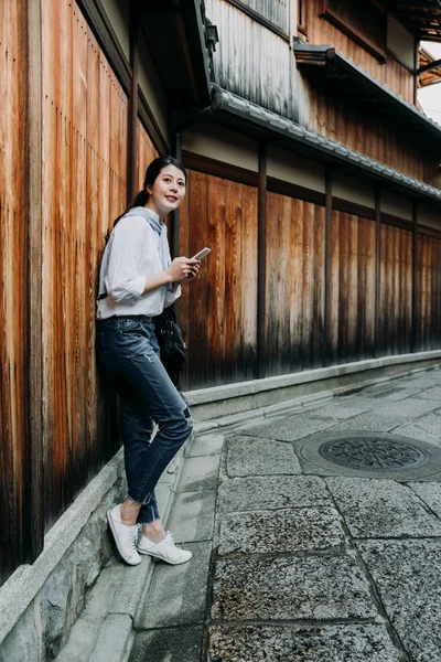 Young Japanese Girl Holding Mobile Phone Relying Wooden Wall Waiting — Stock Photo, Image