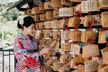 pembe kimono hırka ayakta ahşap tahta dolu dua eden duvarın yanında Japon kadın üzerinde asılı istiyor. geleneksel kıyafet bez kartı gracing üzerinde diğer umut okuma genç kız.
