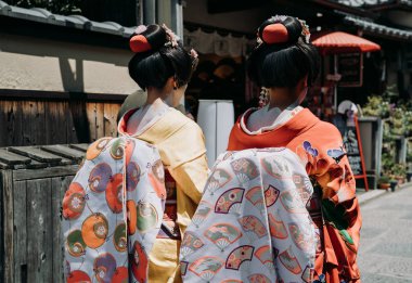 arkadan görünüşü Gion Kyoto Japonya'da bir sokakta yürüyen iki maiko geyşa. Japon kızlar geleneksel bez kimono inanılmaz makyaj ve saç ile eski şehirde güneşli günde elbise.