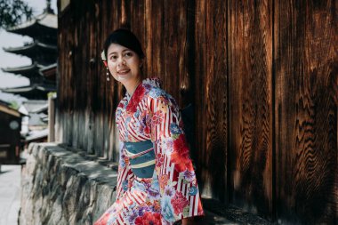 renkli kimono elbise yasaka pagoda içinde geçmiş ile ahşap duvar güvenerek ağaç gölge altında oturan zarif Asyalı kadın. sokak giyim geleneksel bez üzerinde rahatlatıcı gülümseyen genç kız.