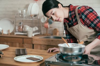 yemek pişirmeye Genç Çinli kız önlük brülör dönüm içinde. Sevgililer günü hediyesi koca için için el yapımı çikolata tatlı eritmek için önlük açık soba yanıyor kadın. zarif kadın hazırlanan hediye