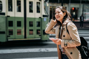 üniversiteli kız çalışma hafta sonu tatil günlerinde yurtdışı gezi. kadın genç yol zebra geçiş planı yol online harita ayakta arama cep telefonu tutuyor. yeşil otobüs ışık tren yoluyla sürücü.