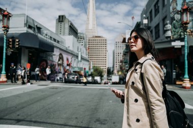 Şehir san Francisco'da yürüyüş smartphone kullanarak gülümseyen Genç Asyalı kadın çok güzel. mutlu kadın modeli açık havada mahallesinde gezi zarif güneş gözlüğü takıyor. Transamerica Pyramid arkada.