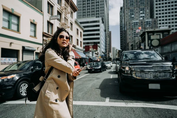 elegant office lady walking on zebra cross going to work. young businesswoman in casual wear holding cellphone on road in busy street area in san francisco usa. girl using mobile phone text sms.