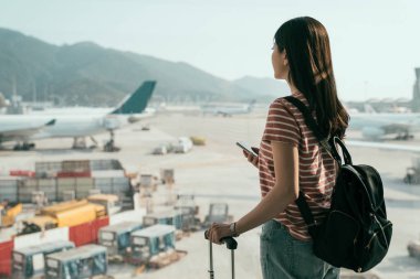 genç kız yoğun uçak önlük ayakta lounge alanı için yürüyüş salonunda cep telefonu sırt çantası ve Bagaj tutan pencere yakınındaki görünümünü görmek. kadın arama online harita hong kong Havaalanı kapıya seyahat