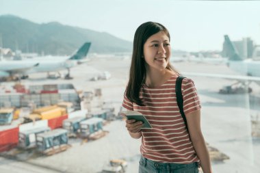 Gençlerin tatil yolculuğun başlangıcı. Pencere Havaalanı lounge yatılı bekleyen uçakları konusunda ise yakın duran güzel Asyalı kadın. Holding pasaport gülümseyen ve pass heyecanlı yatılı Bayan.