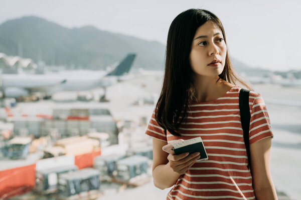 Traveler woman plan and backpack see the airplane at airport glass window. Asian female tourist hold bag and passport board pass near luggage in hall airplane departure. Travel and Holiday Concept.
