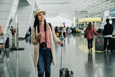 Modern Havaalanı terminal yürüme 20'li yaşlarda genç zarif kadın gezgin. kız arkadaş bulma rahat tarzı giyim eşyası Bagaj çanta taşıyor mesajlaşma halk için wifi alanında akıllı telefon app kullanarak