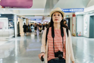 Kendine güvenen kadın backpacker fotoğrafçı Bagaj havaalanında yürüyüş tutarak kamera taşıyordu. Genç Asyalı kadın Gezgin hasır şapka varış hedef gümrük Başlat onu gezi geçmek için çıkıyor.