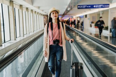 Çinli kız Gezgin Uluslararası Havalimanı terminal uzun yatay yürüyen merdiven üzerinde yürüyen kamera ile. Genç Asyalı kadın turist el Bagaj heyecanlı etrafa geçit taşıma tutarak.