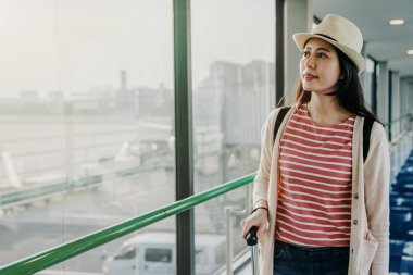 Yolcu uçakları hava kapıya yatılı jetway Havaalanı'nda köprü. geçit üzerinde uçak için yürüyüş bavul tutan genç Asyalı kadın gezgin. zarif Bayan dışında pencere önlük tarafından gezi.