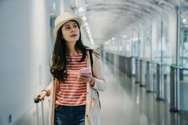 bavul Havaalanı salon ile yürüyen kadın Havaalanı pencere. Asyalı kız Gezgin Bagaj ve cep telefonu arama online web sitesi havayolu kalkış uçuş yatılı kapısı ile