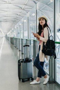 Smartphone Havaalanı Uçak uçuş kalkış zamanı bekleyerek binada mutlu gülümseyerek kullanarak tam uzunlukta Asya hanım. Asyalı kadın yanıt e-posta telefon ayakta bavul ile çalışma.
