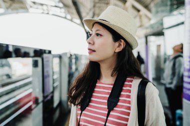 Çanta ile genç Asyalı kız portresi paketi kapısı demiryolu yakınındaki metro platformda. Genç kadın, hasır şapka Havaalanı bekleyen tren metronun Tayvan olacak. güzel turist Bayan ayakta.