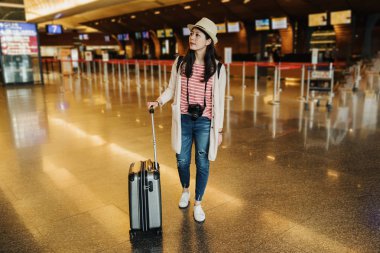 ciddi genç Çinli kadın tam uzunlukta doğru yön Havaalanı'nda bilgi panosunda arıyor. Asyalı kız Gezgin lobi çantada Check-in arka planda sayaç yakın duran.