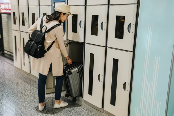 full length female chinese tourists use lock box. new business locker self service storage Mass Transit system for help people and travelers. beautiful girl holding suitcase luggage standing machine.