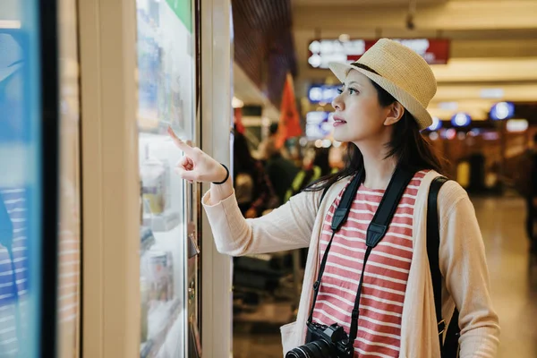 Asya seyahat kadın fotoğrafçı kalkış kapısı uçuşta uçak beklerken havaalanında modern imkanları kullanarak. genç kız sağ el parmak işaret seçme snack içecekler satın almak.