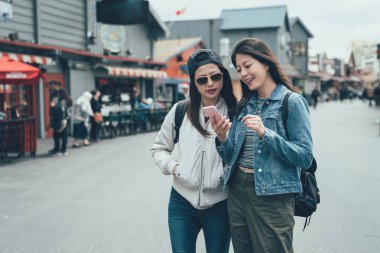 iki genç Asyalı kadınlar arkadaş turist açık çiftçi pazarda eski Fisherman's Wharf monterey duran cep telefonu üzerinde online Haritaya benziyor. gülümseyen kız kız sohbet cep telefonu hakkında konuşun.