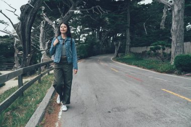 Yalnız dağ karayolu üzerinde bahar bulutlu yürüyüş Asyalı kız backpacker gülümseyen tam uzunlukta. Vintage tarzı genç bayanın forest yakınındaki yolda. mutlu zarif Çinli kadın 17 mil sürücü Kaliforniya üzerinde.
