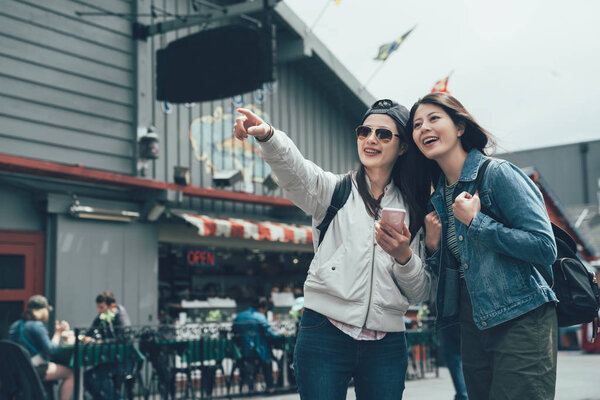 group of asian chinese lady backpacker looking cellphone online map finger pointing searching direction while going to next sightseeing spot. young girls visit Old Fishermans Wharf shopping outdoor.