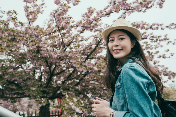 Girl backpacker standing by cherry blossom — Stock Photo, Image