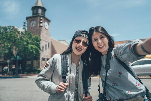 friends hug taking self picture over clock tower