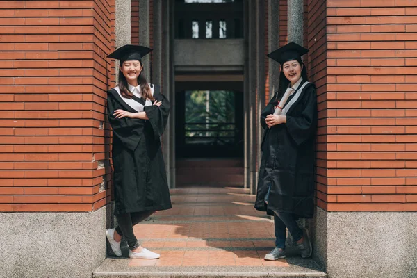 Mujeres graduadas de pie contra la pared de ladrillo rojo —  Fotos de Stock