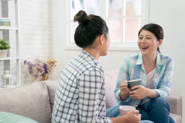 Kadınlar kanepede rahatça otururken gülüyorlar.