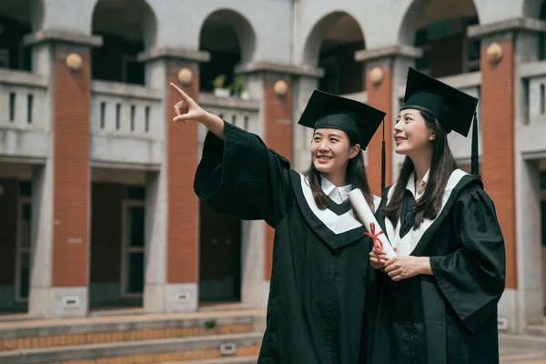 Dos graduados universitarios con diploma apuntando hacia arriba —  Fotos de Stock