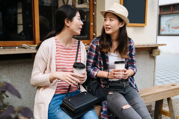 Sisters sitting on wood bench outside cafe shop — Stock Photo, Image