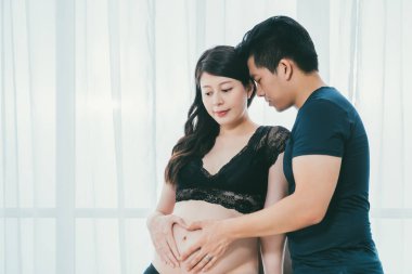 Asyalı adam hamile karısını kucaklamaktan zevk alıyor.