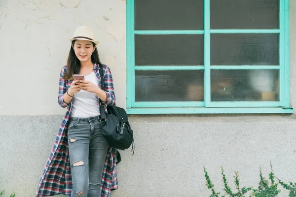 Beyaz duvara yaslanan bir kadın cep telefonuyla mesajlaşıyor. — Stok fotoğraf