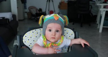 Komik bir çocukla güzel bebek Yün şapka baş, şirin altı aylık erkek bebek yüksek sandalye üzerinde renkli. Görünümü - Dci 4 k çözünürlüklü kapatın