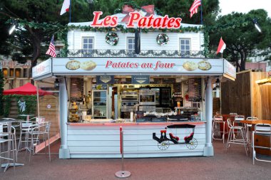 Monte-Carlo, Monaco - December 13, 2018:  Illuminated Christmas Fair Kiosk Market Stall Selling Traditional French Food Hot Potatoes In The Christmas Village. Monaco Christmas Market 2018 In The French Riviera, Europe