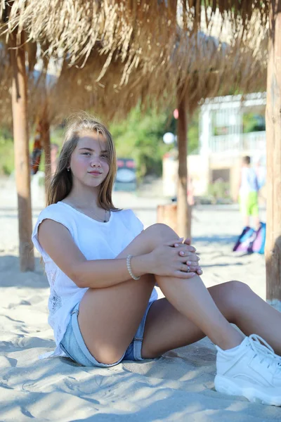 Bonito jovem loira menina sentado no o branco areia praia — Fotografia de Stock