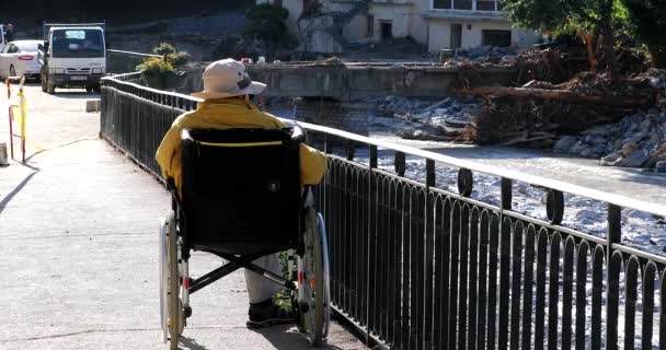 Breil-Sur-Roya, Frankreich - 8. Oktober 2020: Alter Mann im Rollstuhl betrachtet die Sturmschäden In Breil-Sur-Roya, einem Dorf, das von der Überschwemmung des Flusses Roya, Europa, überschwemmt wurde - DCi 4K Resolution