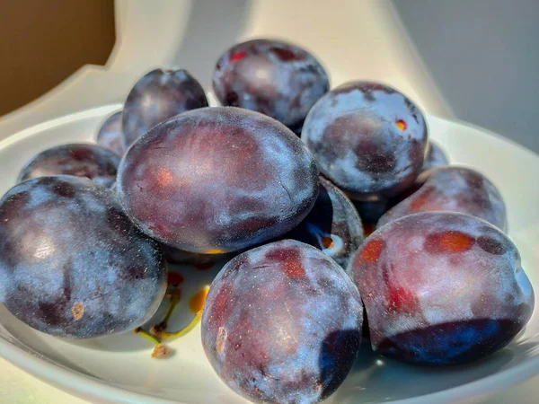 薄明かりの下の白い皿に紫の梅を熟す — ストック写真