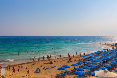 Ayia Napa, Kıbrıs - 06 Eylül 2019: Turistlerle dolu kalabalık plaj. Kumsalda mavi şemsiyeler.