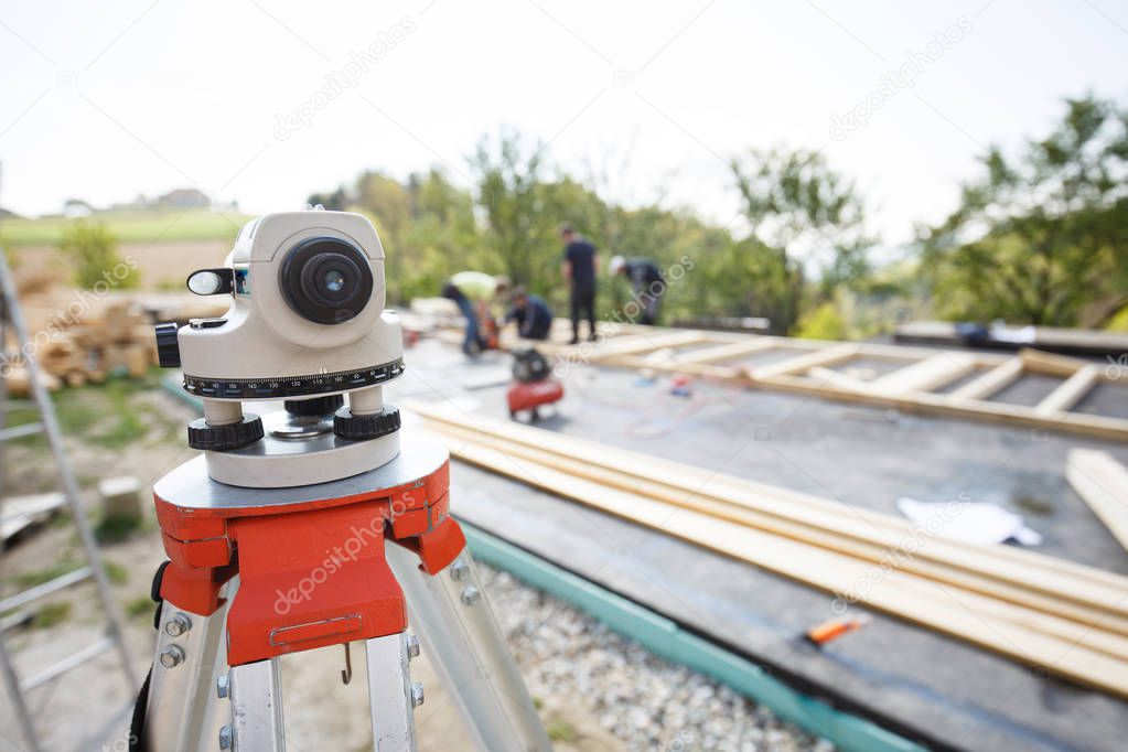 Theodolite measuring angles and positions of modules of prefabricated house. Building industry, carpentry concept with workers in the background erecting the frame.