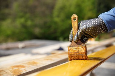 Bir fırça ahşap yüzey üzerinde tutarak, dış etkiler için ahşap koruma ve ayrışma ressam. Marangozluk, ahşap tedavi, iş, ev geliştirme, -it-yourself konsepti zor.