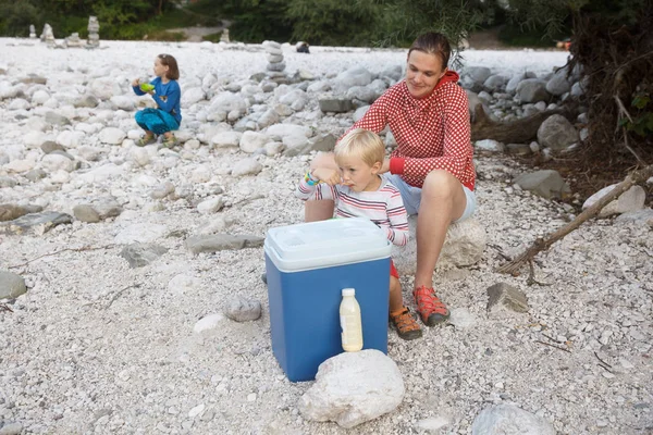 Família fazendo um piquenique na natureza fora de uma caixa legal, sentado na margem do rio . — Fotografia de Stock
