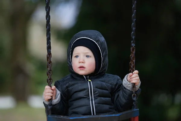 Sad, worried little boy swinging by himself, left alone unattended, looking for parents. — Stock Photo, Image