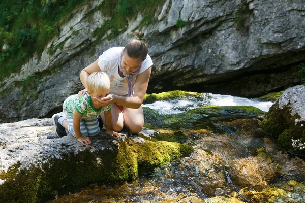 Moeder met zoon drinkwater uit een pure, frisse en koele bergstroom op een familie-uitstapje. — Stockfoto