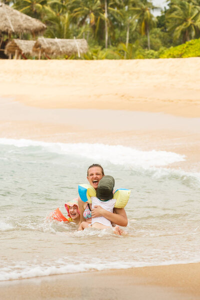 Mother enjoying a tropical beach, playing in the waves with her children. 