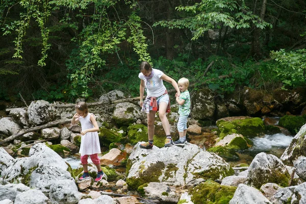 Mère avec des enfants qui s'amusent, jouant près d'un ruisseau de montagne en été . — Photo