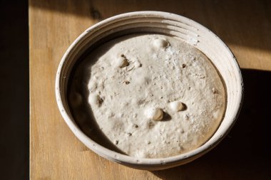 Sourdough bread proofing in a basket with visible gas bubbles. Homemade baking.  clipart